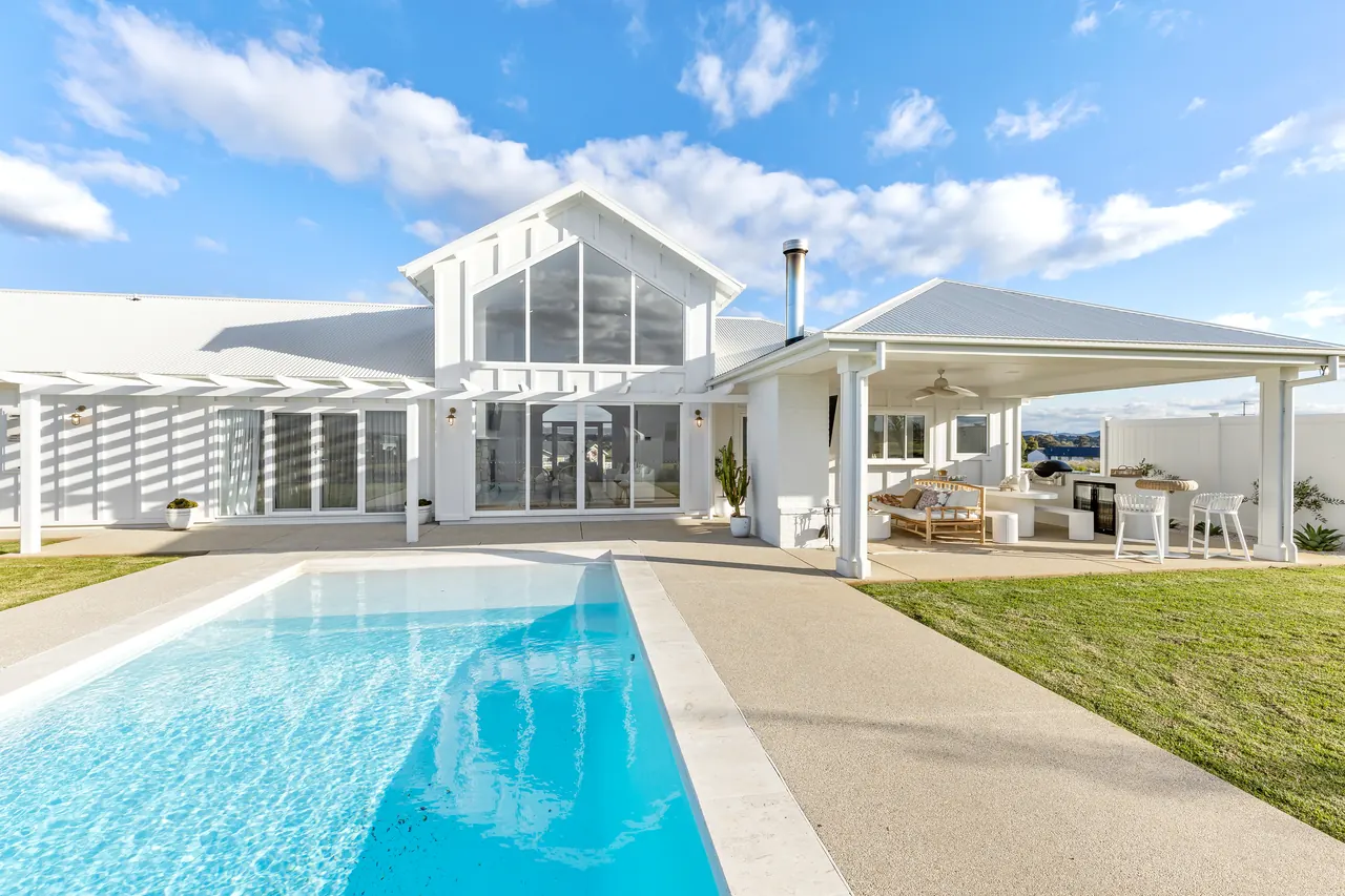 Pool and gabled rear facade of a white rural home