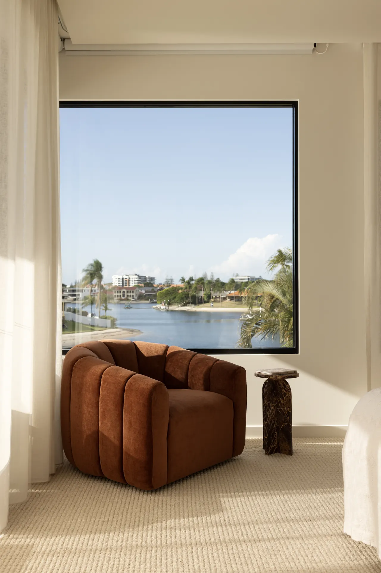 Rust velvet armchair beside a picture window framing the water